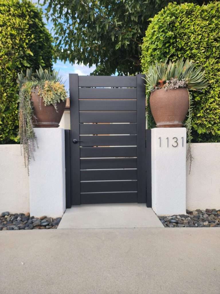 Dark aluminum horizontal-slat pedestrian entry gate framed by planted stucco address pillars in Thousand Oaks, CA