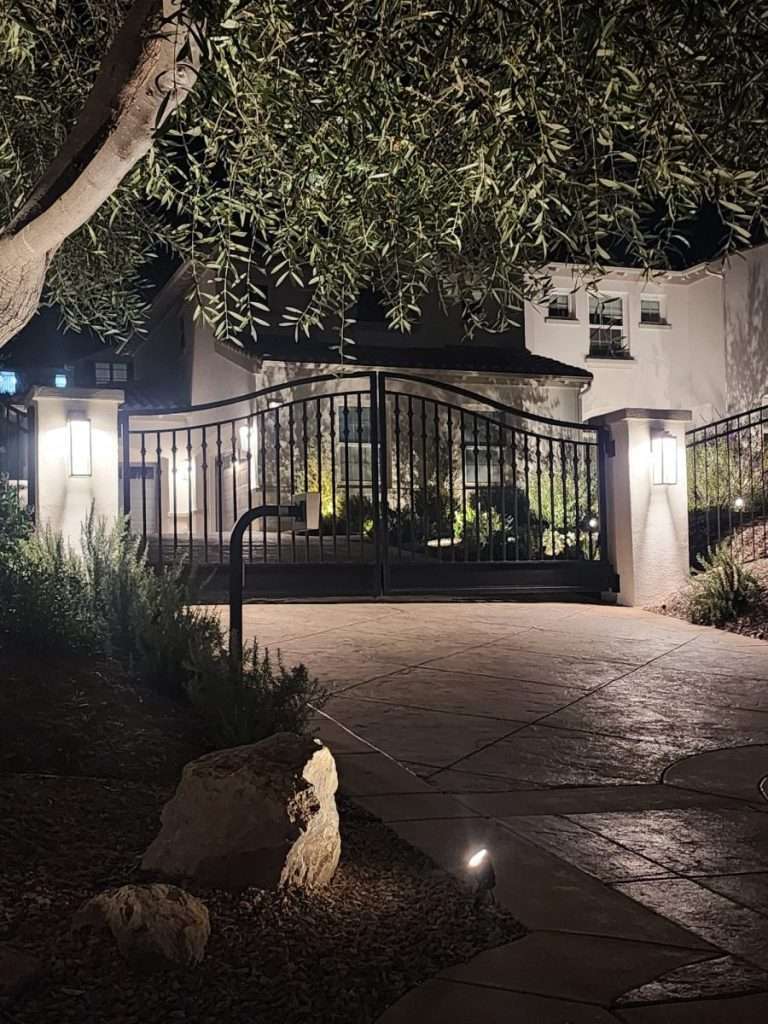 Arched ornamental iron driveway gate lit at night between stone pilasters in Camarillo, CA