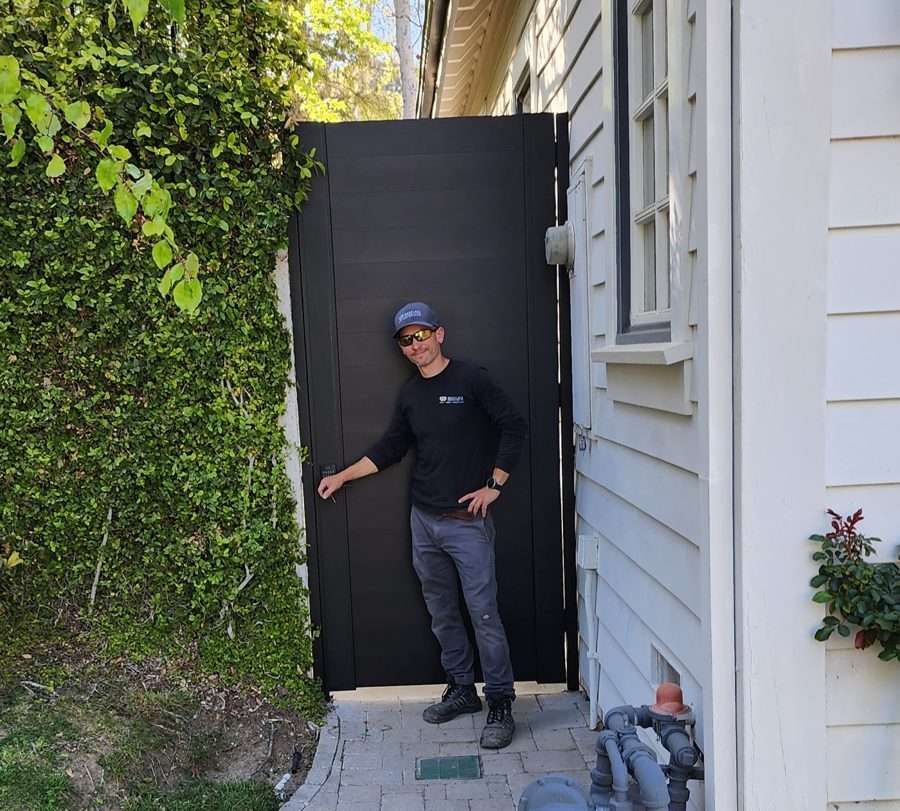 Full-privacy black aluminum gate with horizontal slats beside a shiplap-sided home, with a paver walkway leading to it, built by Westlake Dream Gates